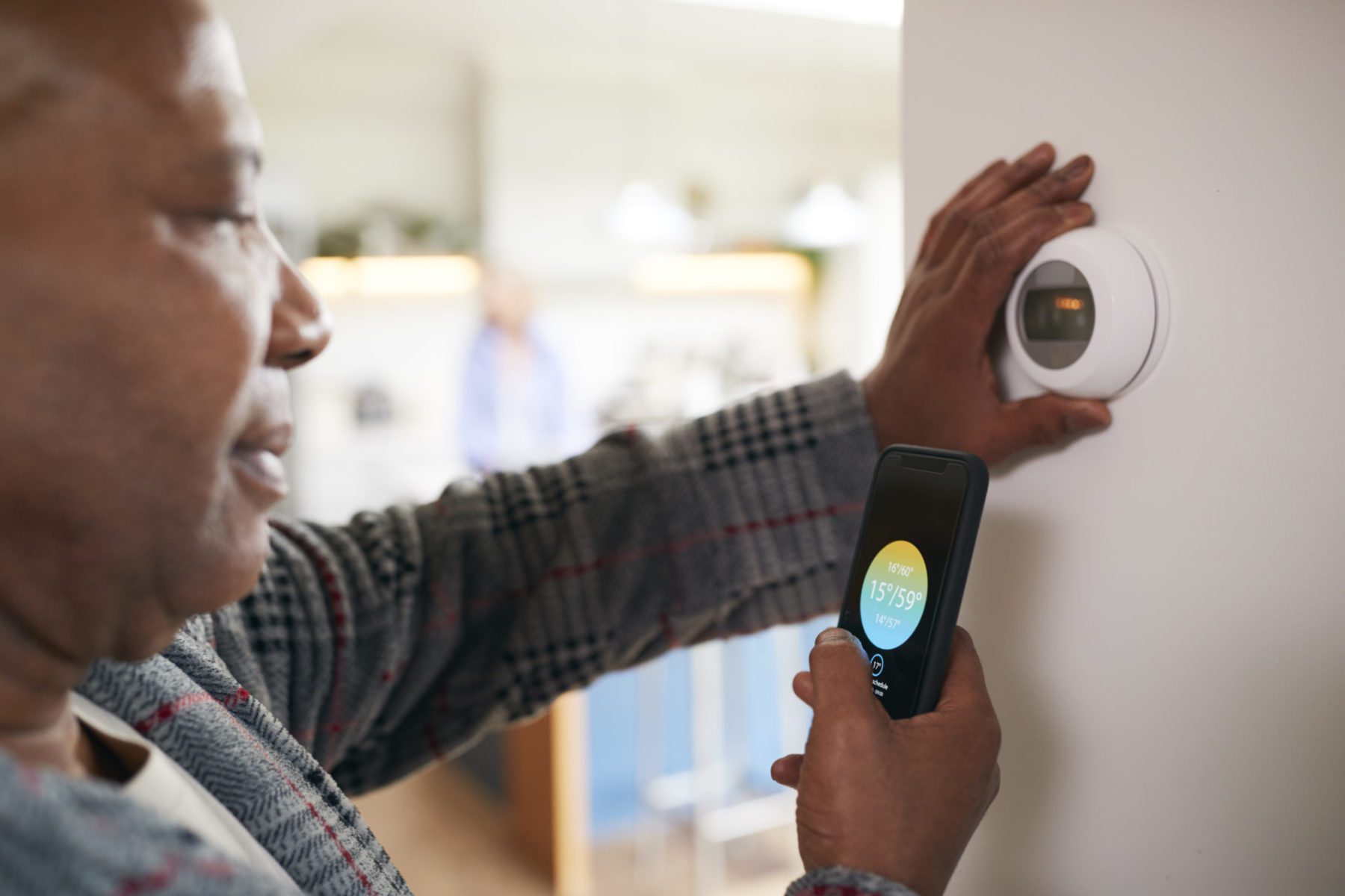 Man Using App On Phone To Control Smart Thermostat At Home